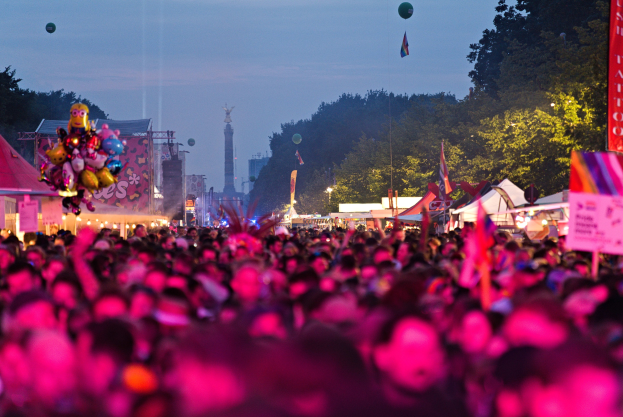 Eine große Menge bei einem nächtlichen Musikfestival mit bunten Lichtern, Ballons, Zelten, Bannern, Fahnen, Bäumen, einem Turm und einem sternenklaren Himmel im Hintergrund.