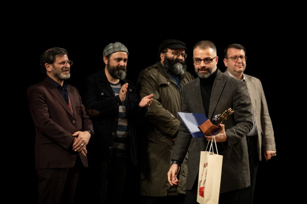Eine Gruppe von Männern auf einer Bühne, einer hält eine Tasche und eine Trophäe, feiernd bei der Eröffnung der Berlinale.
