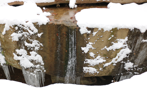 Ein kleiner Wasserfall ergießt sich über eine steinige Klippe, die mit reinem, unberührtem Schnee und glitzerndem Eis bedeckt ist und so eine schöne Winterszene schafft.