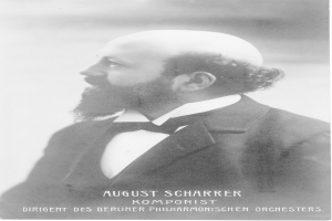 Ein Schwarz-Weiß-Foto von August Scharrer, einem deutschen Komponisten, der einen Blazer und eine Schleife trägt, mit Text am unteren Bildrand.