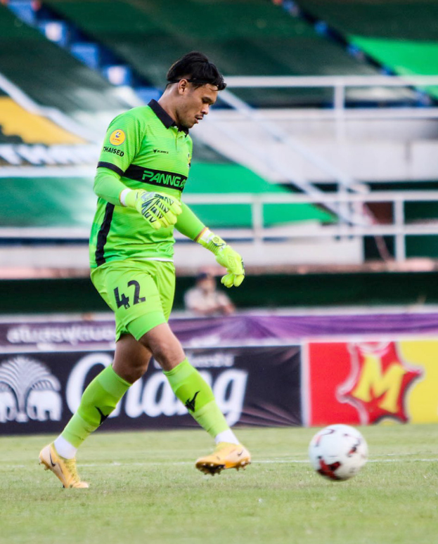 Ein Mann in einem grünen Torwarttrikot schießt einen Fussball auf einem Rasenfeld in einem Stadion, mit Bannern im Hintergrund, die "Chivas USA vs Mexico City, 3-1, Copa Libertadores" anzeigen.