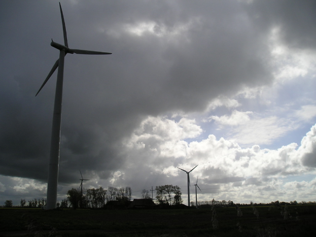 Eine Landschaft mit Windmühlen, Bäumen mit Zweigen und Blättern, Wolken am Himmel und einem Haus in der Ferne.