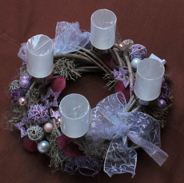 Ein beleuchtetes Weihnachtsgesteck mit Kerzen und Schmuck auf einem Holztisch, umgeben von Bändern und Sternen in einer warmen, festlichen Atmosphäre.