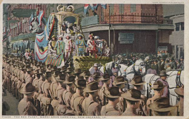 Eine alte Postkarte zeigt einen Karnevalsumzug in New Orleans mit einem geschmückten Wagen, Reiter und Zuschauern am Straßenrand, mit der Beschriftung "The Rex Float, Mardi Gras Carnival, New Orleans" darunter.