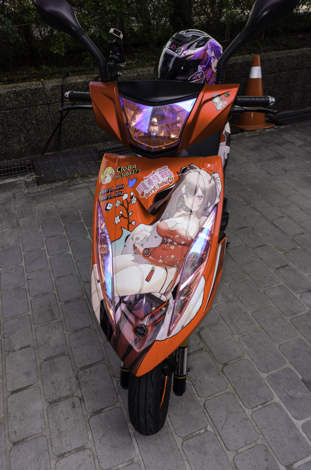 Ein oranger Roller mit Helm auf der Straßenseite geparkt, mit einem Verkehrskegel, einer Wand und Bäumen im Hintergrund.