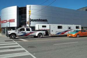 Ein Polizei-Lkw steht vor einem Gebäude mit Text darauf, mit einer Verkehrsampel mit Stange und Drähten im Vordergrund und Bäumen und einem klaren blauen Himmel im Hintergrund.