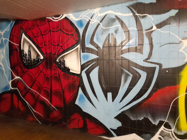 Mural von Spider-Man in rot und blauem Kostüm mit Webmuster und Spider-Logo auf einer Gebäudewand, mit breiteren Augen und leicht geöffnetem Mund.