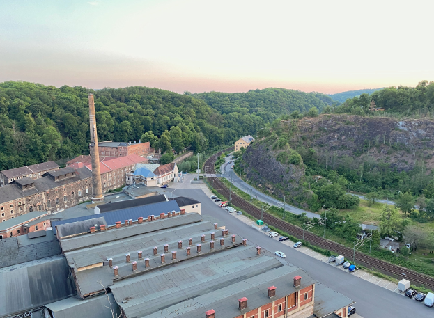 Luftaufnahme einer Stadt mit dichtem Gebäudebestand, Straßen voller Fahrzeuge, Strommasten, vereinzelten Bäumen, fernen Hügeln und einem bewölkten Himmel, die an ein Kohlebergwerk erinnern.