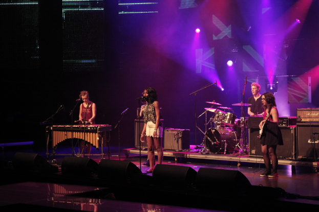 Vier Personen auf einer Bühne mit Musikinstrumenten und einem Mikrofon.