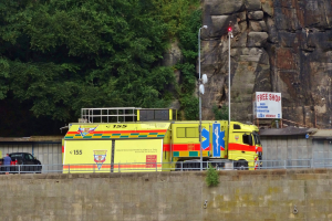 Ambulanz am Rande einer Stra├če neben einer Klippe geparkt, mit verschiedenen Gegenst├Ąnden und B├Ąumen im Hintergrund.