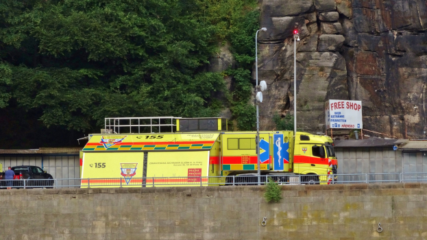 Ambulanz am Rande einer Stra├če neben einer Klippe geparkt, mit verschiedenen Gegenst├Ąnden und B├Ąumen im Hintergrund.