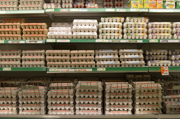 Ein Supermarktregal mit mehreren Eiertrays neben verschiedenen Früchten, Gemüsen und anderen Lebensmitteln.