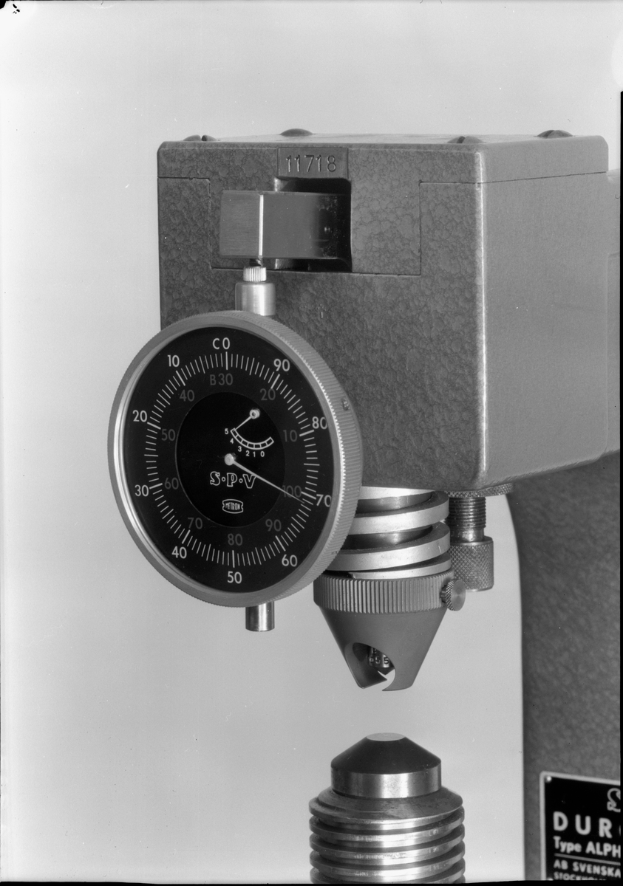 Ein Schwarz-Weiß-Foto eines Messgeräts, einer Maschine zur Dickenmessung eines Metallstücks.