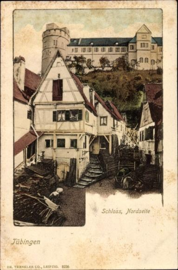 Eine alte Postkarte, die ein Gebäude mit einem Turm im Hintergrund zeigt, umgeben von Bäumen unter einem klaren blauen Himmel, mit der Aufschrift "Tübingen, Deutschland" unten.