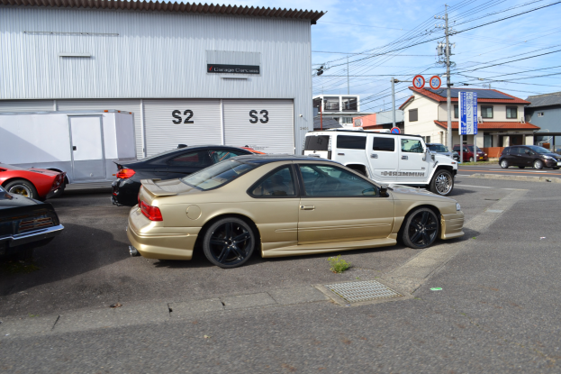 Ein goldfarbener Wagen auf einer Straße mit anderen Fahrzeugen vor Häusern unter einem klaren blauen Himmel.