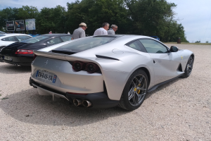 Roter Ferrari 812 Superfast auf der Goodwood Festival of Speed, mit Zuschauern in Mützen und Veranstaltungsbeschilderung im Hintergrund.