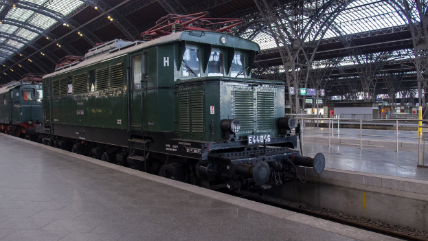 Ein Zug auf Schienen mit Geländern und Planken im Hintergrund, Lampen auf dem Dach und ein Himmel darüber, mit einem Boden und Schienen darunter.