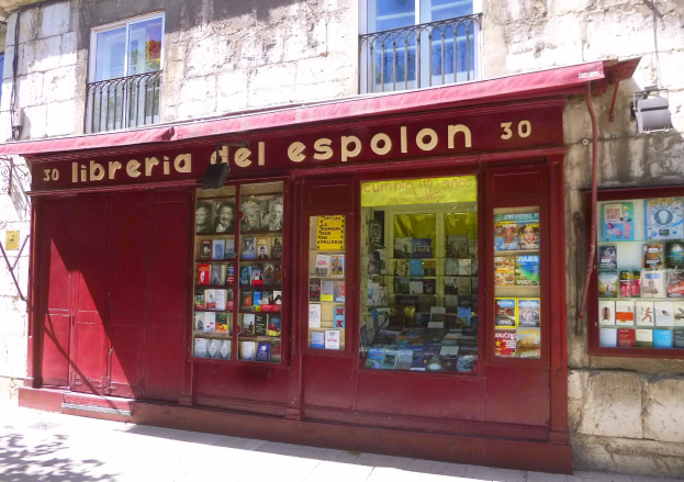 Ein zweistöckiges Gebäude mit einer Schaufensterfront, die ein rotes Vordach trägt, auf dem "Libreria del Espolon" steht und drinnen ordentlich aufgereihte Bücher zeigt.