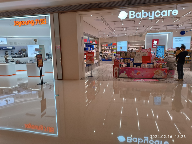 Babycare-Laden im Mall of Asia Einkaufszentrum mit Regalen voller Artikel, Schildern, einem Display, Deckenlampen und einer Gruppe von Menschen umgeben von Spielzeugen.