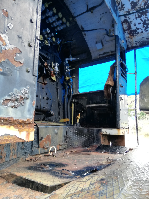 Das Innere einer verrosteten, beschädigten Lkw-Kabine mit Bäumen und einem klaren blauen Himmel im Hintergrund.