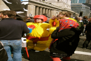 Ein Clown steht in der Mitte des Bildes mit Menschen auf beiden Seiten und Geb├Ąude sind oben sichtbar.