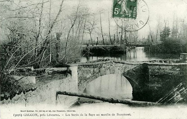 Ein altes Schwarz-Weiß-Foto einer baufälligen Brücke über einen Fluss, flankiert von Bäumen, mit einem Stempel oben und Text unten.