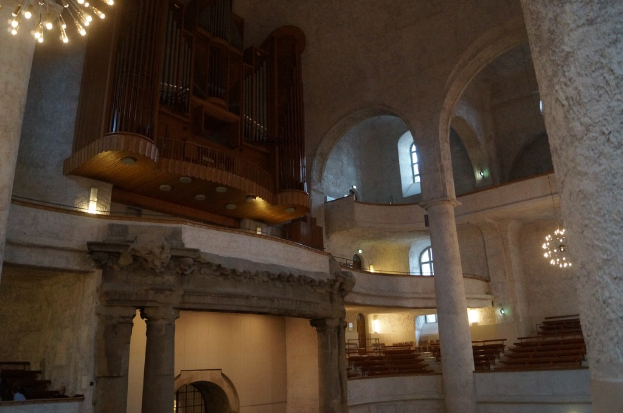 Das Innere eines Gebäudes mit Lampen, Stufen, Säulen, einem hölzernen Gegenstand an der Wand, Fenstern und Türen.