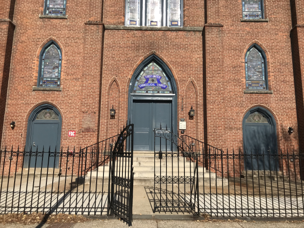 Großes Backsteingebäude mit schwarzem Tor, Fenstern, Türen, Treppen, Geländern und Lampen, als die erste vereinigte evangelische Kirche in Chicago bezeichnet.