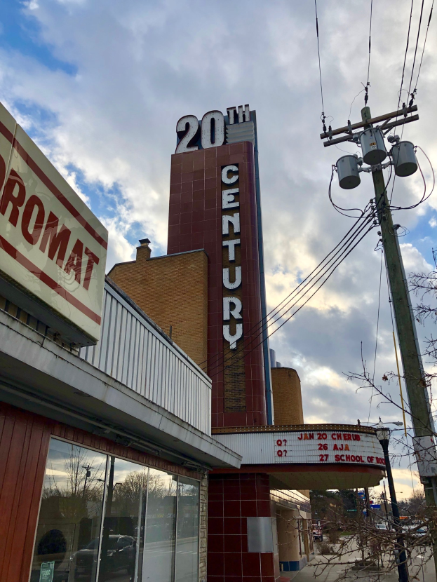 Außenansicht des 20th Century Theatre in Detroit, Michigan, mit Glaswänden, Namensschildern, umgeben von Bäumen und Strommasten mit Drähten, unter einem bewölkten Himmel.