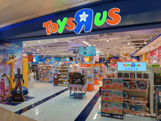 Ein Toys R Us-Laden in einem Einkaufszentrum mit Regalen voller Spielzeuge, einem Namensschild mit Text, Deckenleuchten und einem Wasserzeichen in der rechten unteren Ecke.