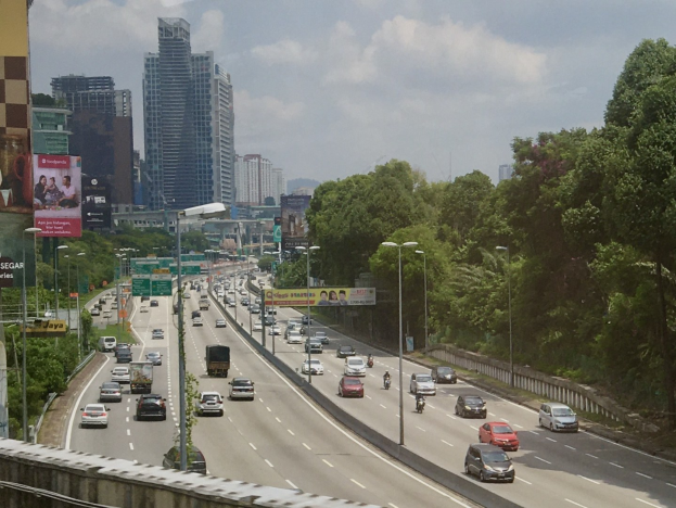 Eine verkehrsreiche Autobahn mit hohen Gebäuden, Straßeninfrastruktur, Bäumen und einem bewölkten Himmel.
