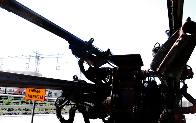 Eine Maschine vorne mit Strommasten, Kabeln, Barrieren, Pflanzen und Himmel im Hintergrund.