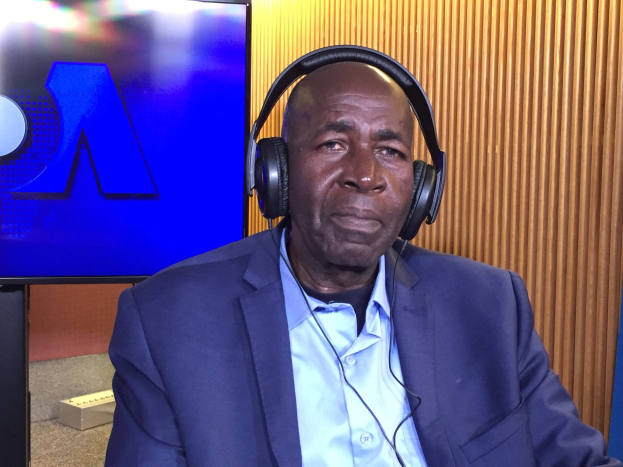 Ein Mann im Anzug mit Kopfhörern sitzt vor einem Fernseher und spricht während einer Diskussion über das Internetverbot in Nigeria, mit einer hölzernen Wand im Hintergrund.