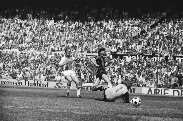 Schwarzes Foto von Männern, die auf einem Feld Füüball spielen, mit Zuschauern im Hintergrund und einer Banner mit der Aufschrift "Bundesliga 1978-79 Ajax 1-1 Hannover 96".
