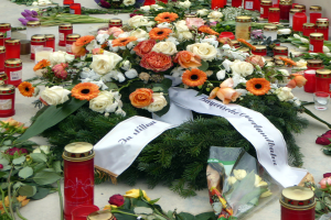 Mahnmal in Berlin mit Blumen und Kerzen vor einer Wand aufgestellt.