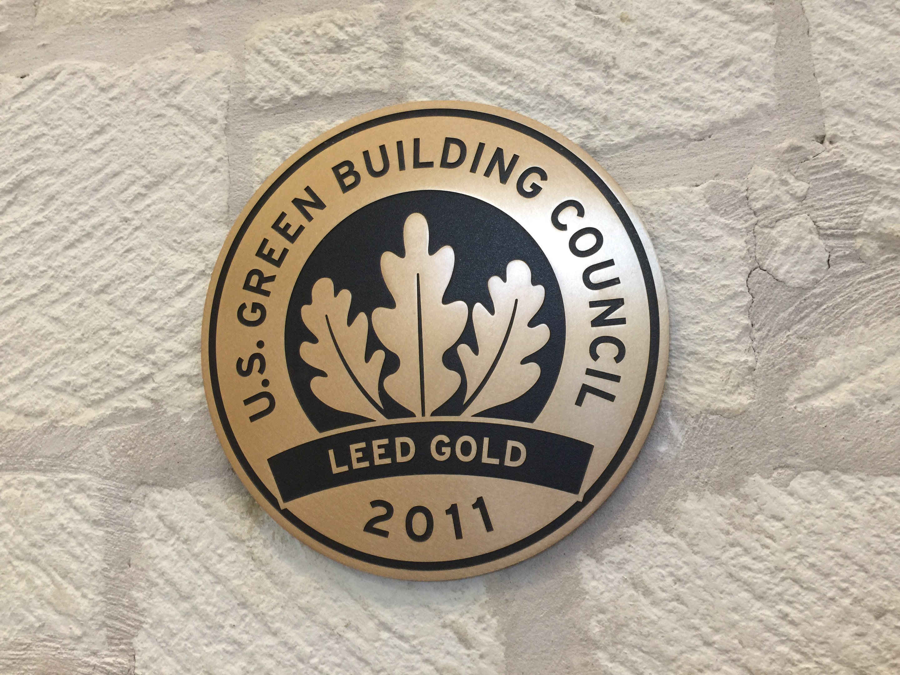 Das Logo des U.S. Green Building Council an der Seite eines Gebäudes, das einen grünen Schild mit weißer Umrandung, fetten schwarzen Text und einen umgebenden Lorbeerkranz zeigt.