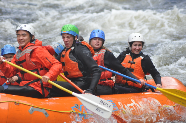 Eine Gruppe von Menschen mit Paddeln sitzt auf einem aufblasbaren Boot auf dem Wasser.