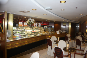 Ein Restaurant-Innenraum mit Tischen und Stühlen, einer Theke mit Blumenvasen, Schildern, einem Ventilator und anderen Gegenständen unter einer von Lampen beleuchteten Decke.