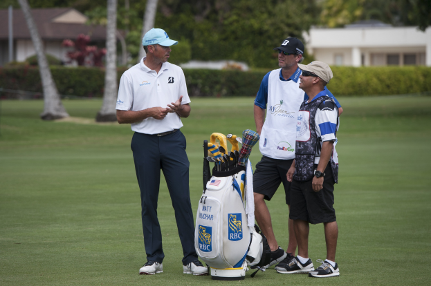 Mannergruppe auf einem grünen Feld mit einem Golfbag und -schlägern im Vordergrund, Bäume, Pflanzen und Gebäude im Hintergrund.