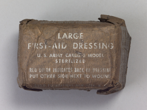 Großes rechteckiges Verbandkasten mit leicht geöffnetem Deckel, beschriftet mit "Großes Verbandmaterial" in fetter schwarzer Schrift.