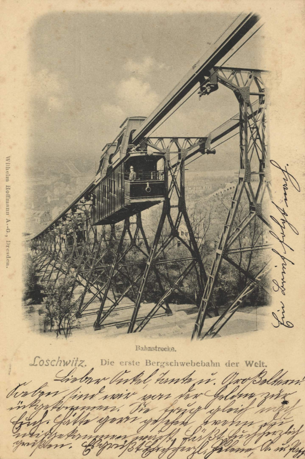 Ein altes Schwarz-Weiß-Foto einer Eisenbahnbrücke mit einem Kran, umgeben von Bäumen und einem bewölkten Himmel, mit Text unten, der lautet: "Bahnstrecka, die erste Eisenbahnbrücke in Deutschland".