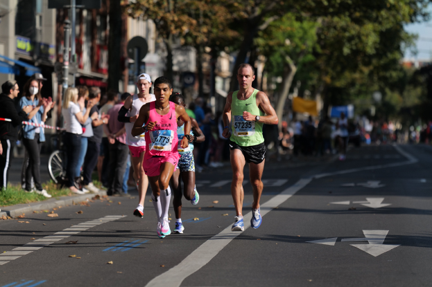 Gruppe von Läufern bei einem Marathon auf einer Stadtstraße, mit Zuschauern und städtischen Elementen im Hintergrund.