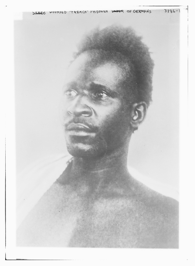 Schwarz-weiß-Foto eines Mannes mit ernstem Gesichtsausdruck, beschriftet mit 'Seneg Verwundeter französischer Gefangener unter Deutschen' oben.