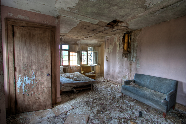 Ein verwüstetes Zimmer mit einer sichtbaren Tür, einer Couch und einem Bett.