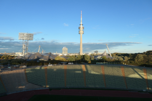 Das Olympiastadion in Berlin, Deutschland, mit dem Fernsehturm im Hintergrund, umgeben von Bäumen, Gebäuden und Lichtern unter einem bewölkten Himmel.