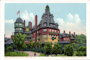 Eine alte Postkarte zeigt das Battery Park Hotel in Asheville, North Carolina, ein großes Gebäude mit einer Fahne oben, umgeben von Bäumen, Pflanzen und Gras, mit einem Weg im Vordergrund und Text unten.