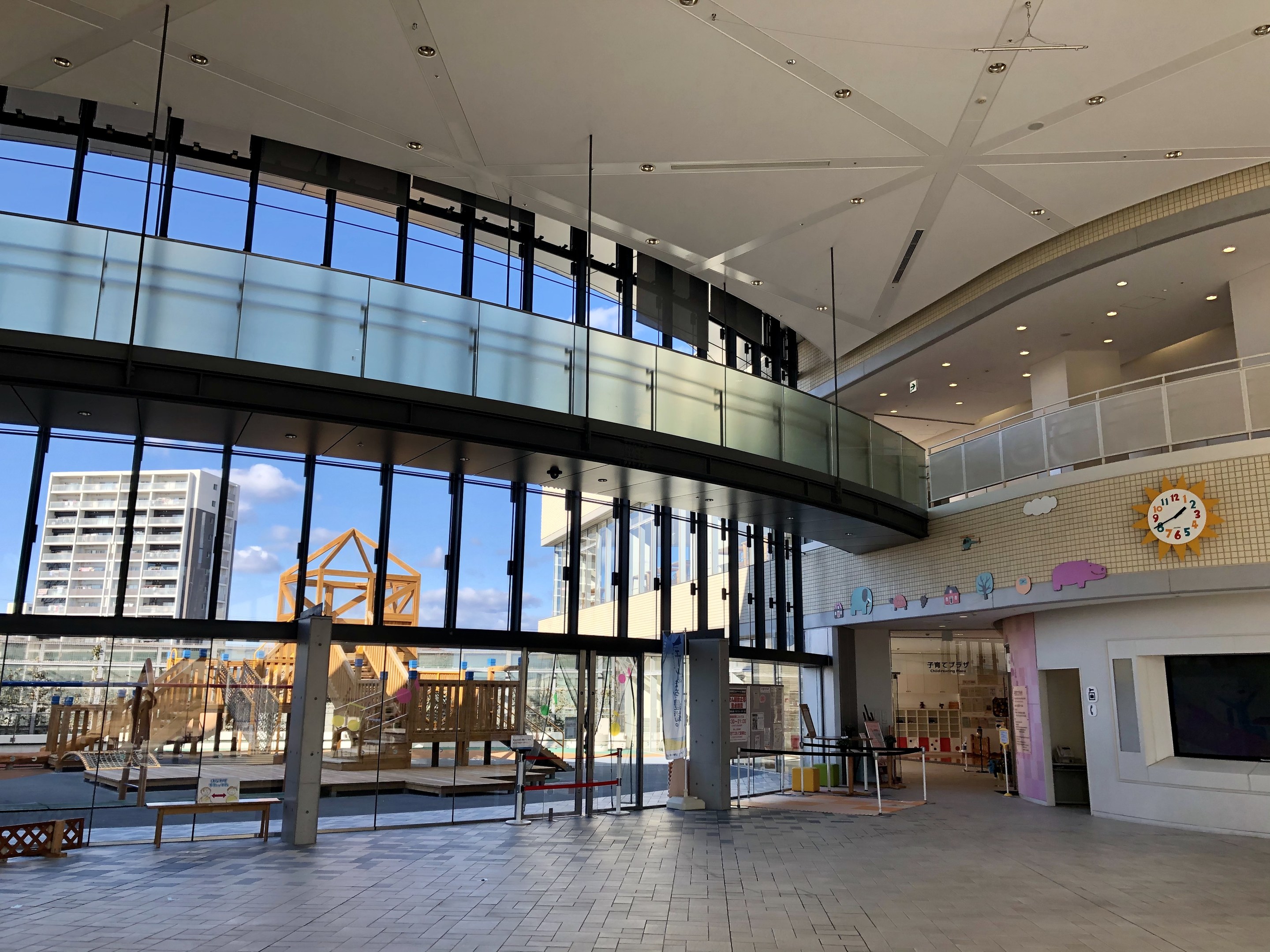 Innenansicht eines gro├čen Geb├Ąudes mit einer Uhr an der Wand, Fernseher, Anzeigebildschirm, h├Âlzernen Gegenst├Ąnden und einem h├Âlzernen Zaun, der als Haupteingang zu einem neuen Kinderspielplatz dient.