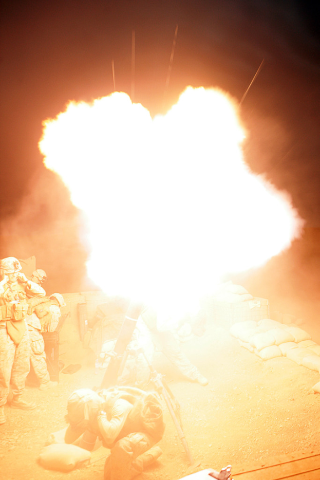 Mehrere Personen in Uniformen und Helmen befinden sich auf einem Gelände mit einigen Taschen, die herumliegen, mit einem Feuer in der Mitte der Szene.