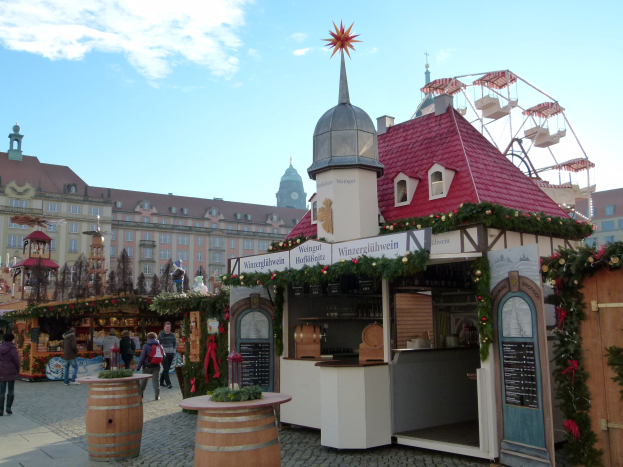 Ein geschäftiger Weihnachtsmarkt in Nürnberg, Deutschland, mit Menschen um geschmückte Buden, festliche Lichter, ein Riesenrad im Hintergrund und eine Tafel auf der rechten Seite.