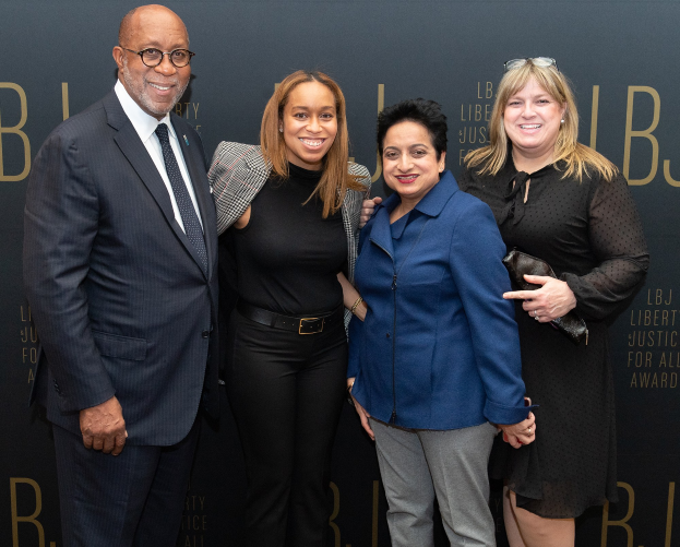 Eine Gruppe von vier Personen auf einem roten Teppich, die lächeln und für ein Foto posieren, mit einem "Liberty Justice for All Awards"-Schild im Hintergrund.